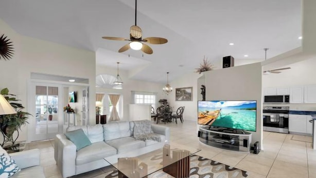 A spacious living room with a large flat-screen TV, a ceiling fan, and a modern kitchen in the background. - Casa de La Vista – Pool & Spa with lakefront view (Cape Coral)