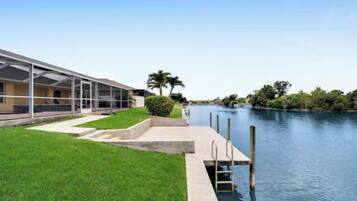 A waterfront property with a grassy lawn, a pool, and a building with a covered patio area.
