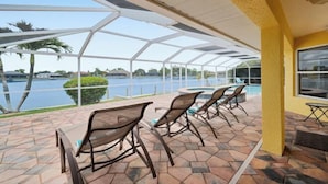 A covered patio with a view of a lake, outdoor seating, and a pool. - Casa de La Vista – Pool & Spa with lakefront view (Cape Coral)