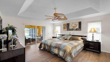 A bedroom with a bed, bedside tables, a ceiling fan, a window with blinds, and a door leading to another room.
