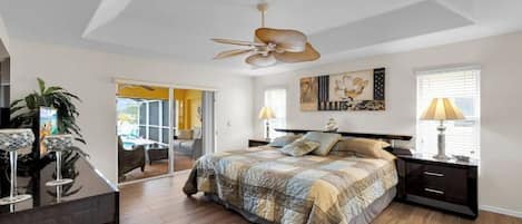 A bedroom with a bed, bedside tables, a ceiling fan, a window with blinds, and a door leading to another room.