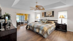 A bedroom with a bed, a ceiling fan, a nightstand, a lamp, and a large window. - Casa de La Vista – Pool & Spa with lakefront view (Cape Coral)