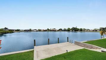 A calm lake with a concrete dock, surrounded by a grassy area and distant buildings.