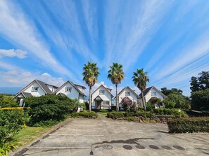 Filas de casas blancas con techos grises, rodeadas de vegetación y palmeras, bajo un cielo despejado.