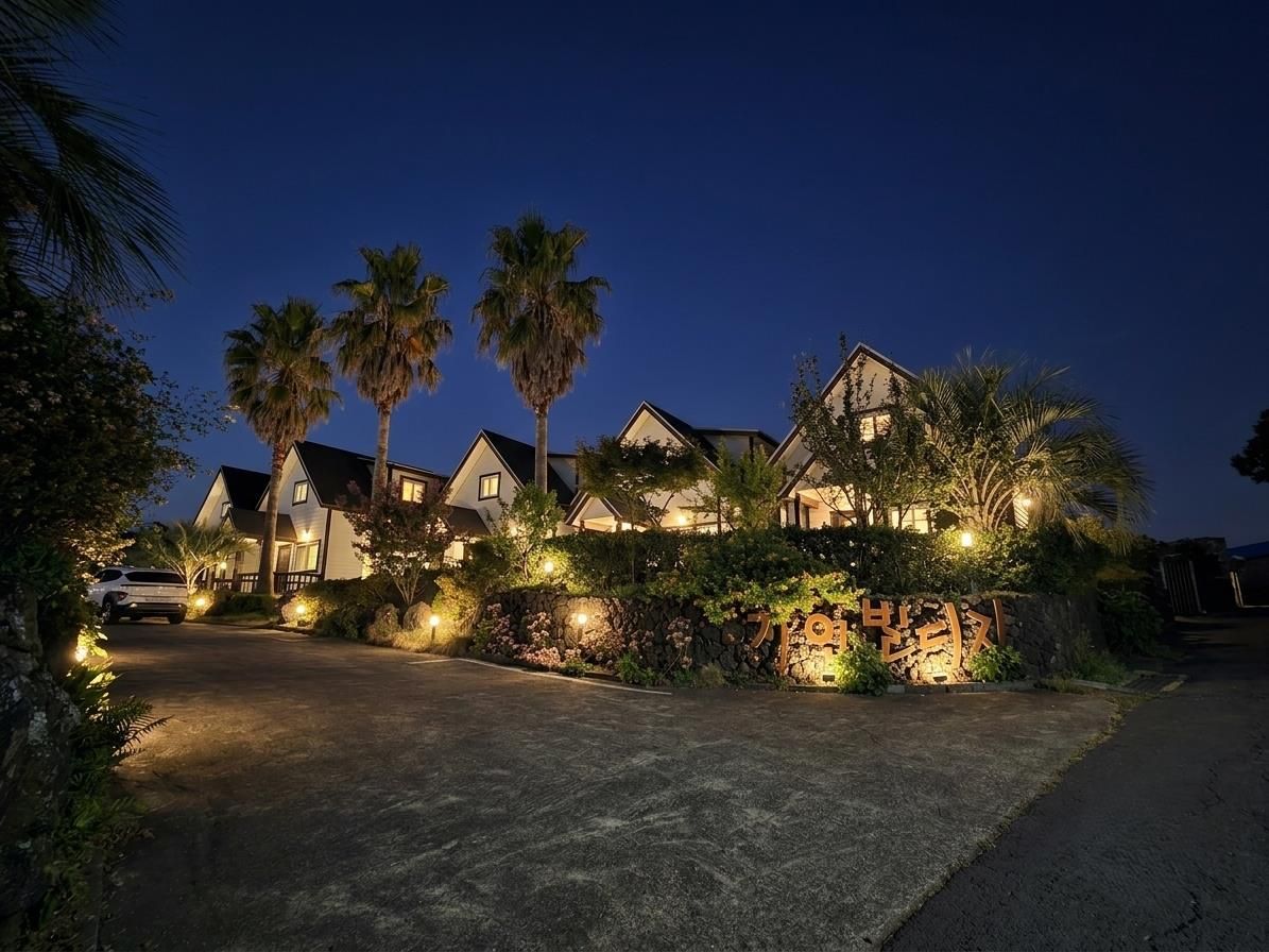 A residential area at dusk with houses, palm trees, and a lit pathway.