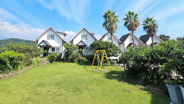 A residential area with multiple houses, a grassy lawn, and a swing set. - Zain Village pension (Seogwipo)