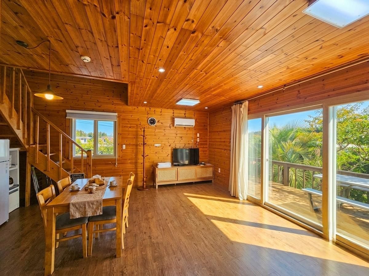 A wooden interior with a dining area, a TV, and a balcony with a view.
