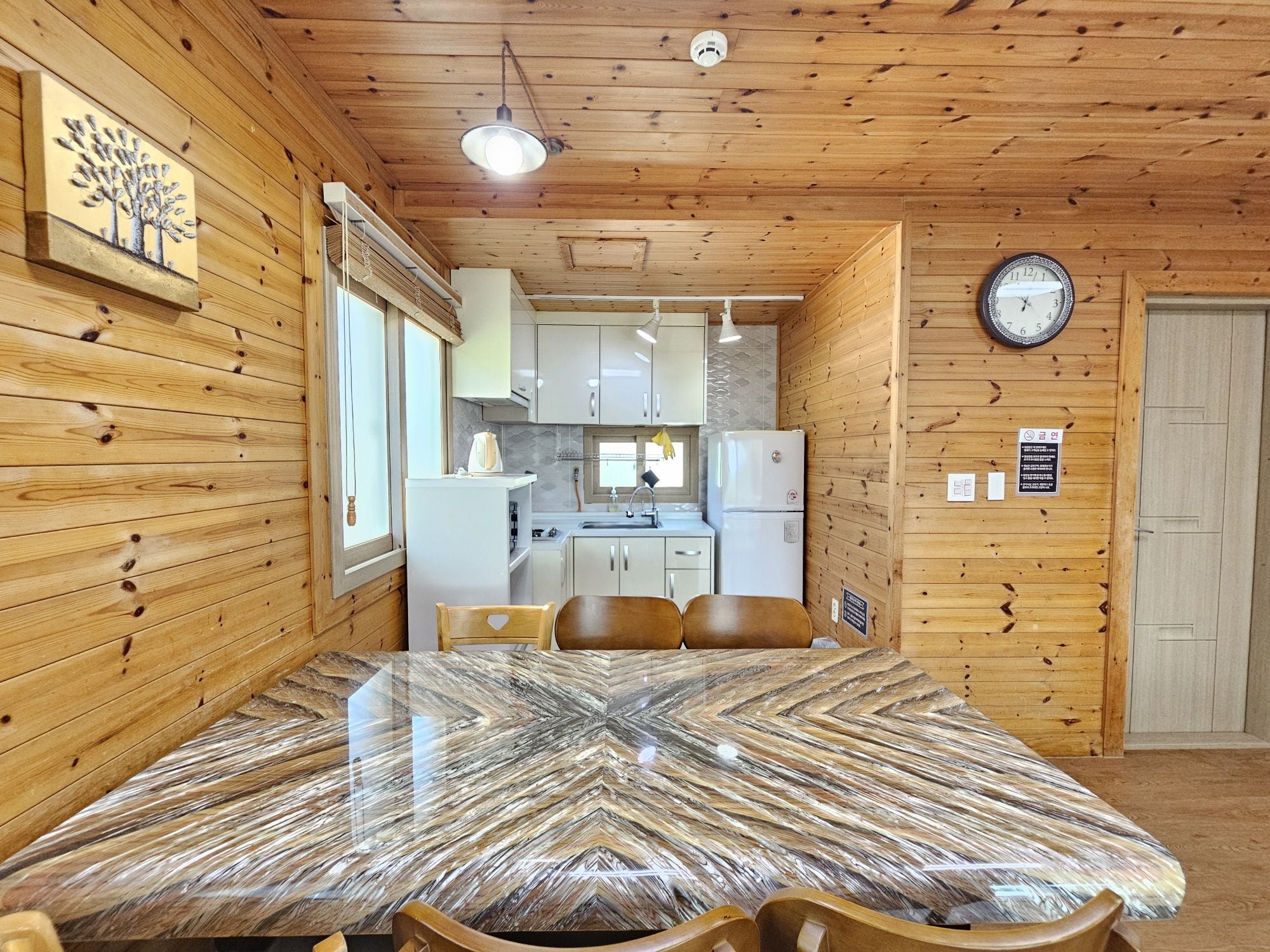 Un interior de madera con una mesa de comedor, sillas, una zona de cocina y un reloj en la pared.