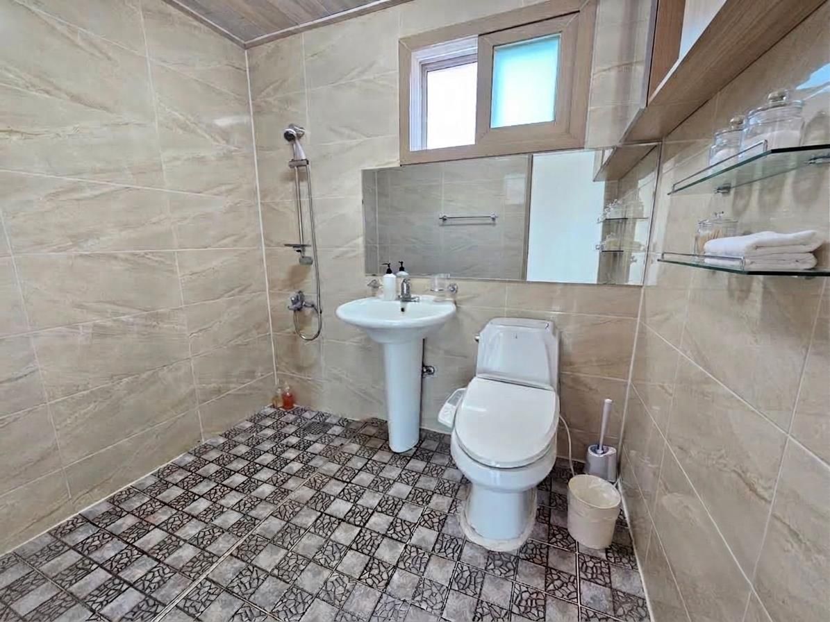 A bathroom with a shower, sink, toilet, and a glass shelf with toiletries.