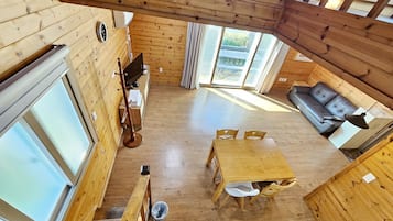 A wooden interior with a dining area, a sofa, a TV, and a window.