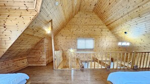 A wooden attic bedroom with two beds, a window, and a staircase. - Zain Village pension (Seogwipo)