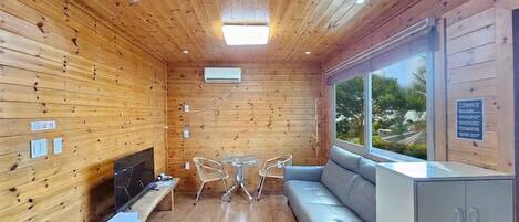 A wooden-paneled room with a sofa, a small table, a television, and a cabinet.