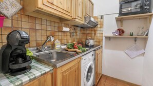 A compact kitchen with wooden cabinets, a washing machine, a coffee maker, and a microwave. - Appartamento La Selva Incantata, Sauze d'Oulx, Italy (Sauze d'Oulx)