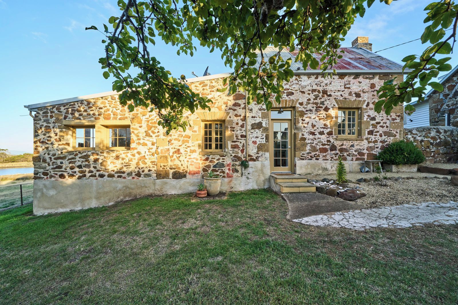 A stone building with a door and windows, surrounded by a grassy area and potted plants.