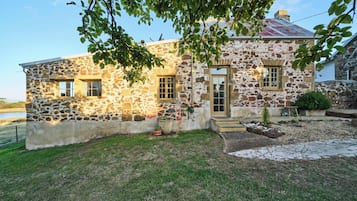 A stone building with a door and windows, surrounded by a grassy area and potted plants.