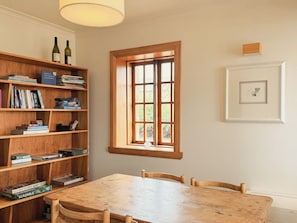 Een kamer met een houten tafel, stoelen, een boekenkast, een raam en een lijst met een afbeelding aan de muur.