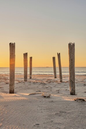 Een strand met houten palen en voetafdrukken in het zand.