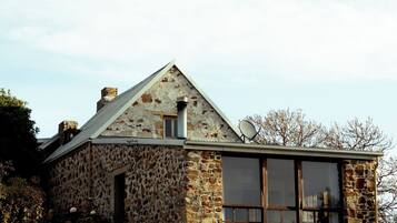 Una casa de piedra con techo a dos aguas, ventanas grandes y una antena parabólica.