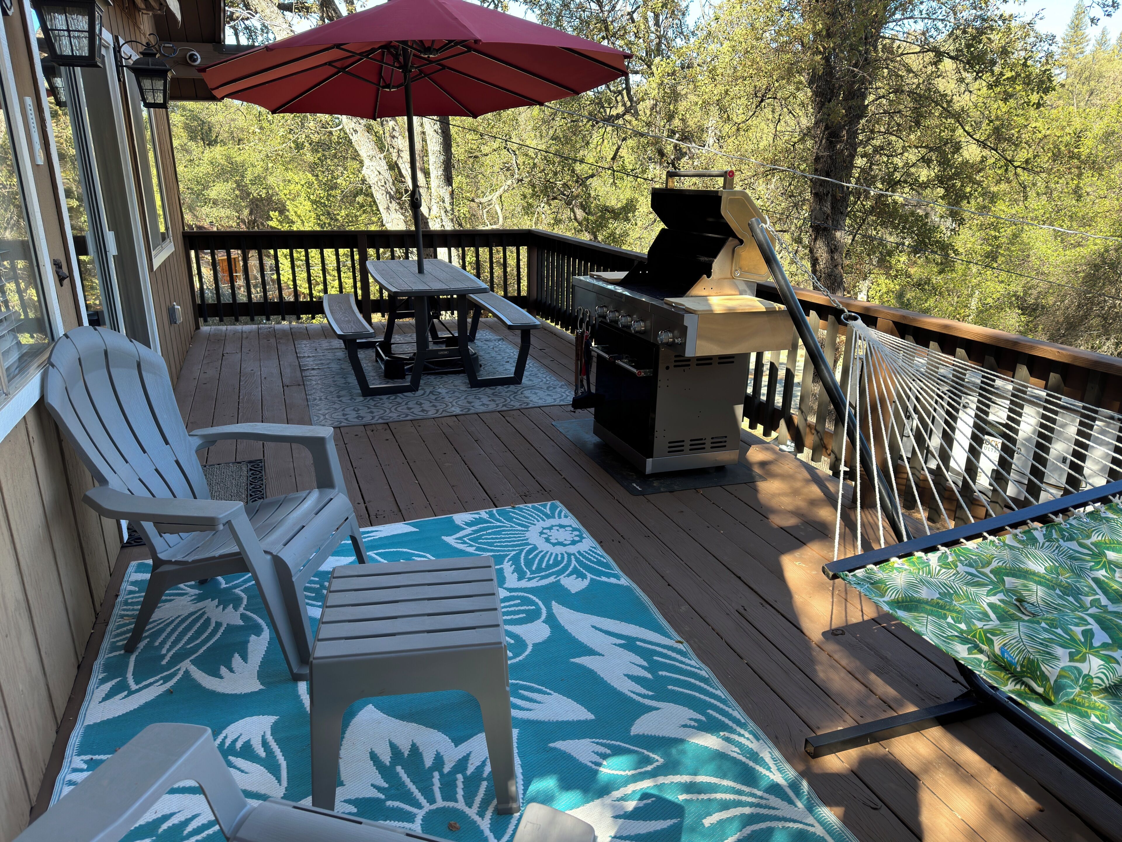 Une terrasse avec un barbecue, du mobilier d’extérieur et un parasol rouge.