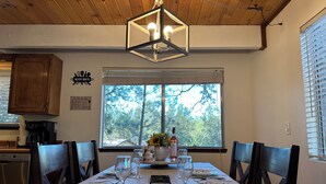 A dining area with a table set for four, a wooden ceiling, and a view of trees through a window.