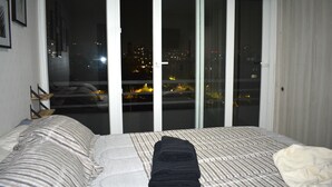 A bedroom with a bed, a window with a view of the city at night, and a sliding door. - Apartamento 2 dormitorios, cerca de lo mas destacado de la ciudad y aeropuerto (Santiago)