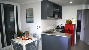 A modern kitchen with a central island, grey cabinets, and a red refrigerator. - Apartamento 2 dormitorios, cerca de lo mas destacado de la ciudad y aeropuerto (Santiago)