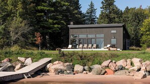 Une cabane moderne dotée de grandes fenêtres, d’une terrasse et offrant une vue sur la forêt environnante.