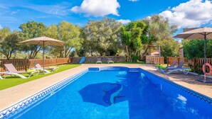 Piscina rettangolare con bordo in mosaico blu, circondata da una recinzione in legno e ombreggiata da due ombrelloni.