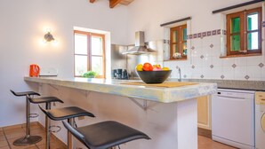 Una cucina con isola centrale, sgabelli da bar, lavastoviglie e una finestra con persiane verdi.