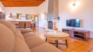 Un soggiorno con divano, un tavolino rotondo con un sottobicchiere in pizzo, camino, televisore e travi in legno al soffitto.