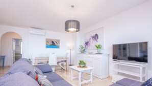 Una sala de estar moderna con un televisor de pantalla plana grande, sofás grises, una mesita blanca y una planta decorativa.