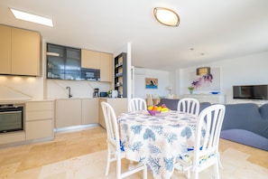 A modern kitchen with white cabinets, a dining table with a floral tablecloth, and a TV in the living area. - BRISA MARINA - Modern seafront apartment in Colònia de Sant Pere - Free Wi-Fi (Artà)