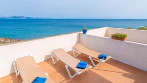 Una terraza con tres tumbonas, una planta en maceta y vista al mar.