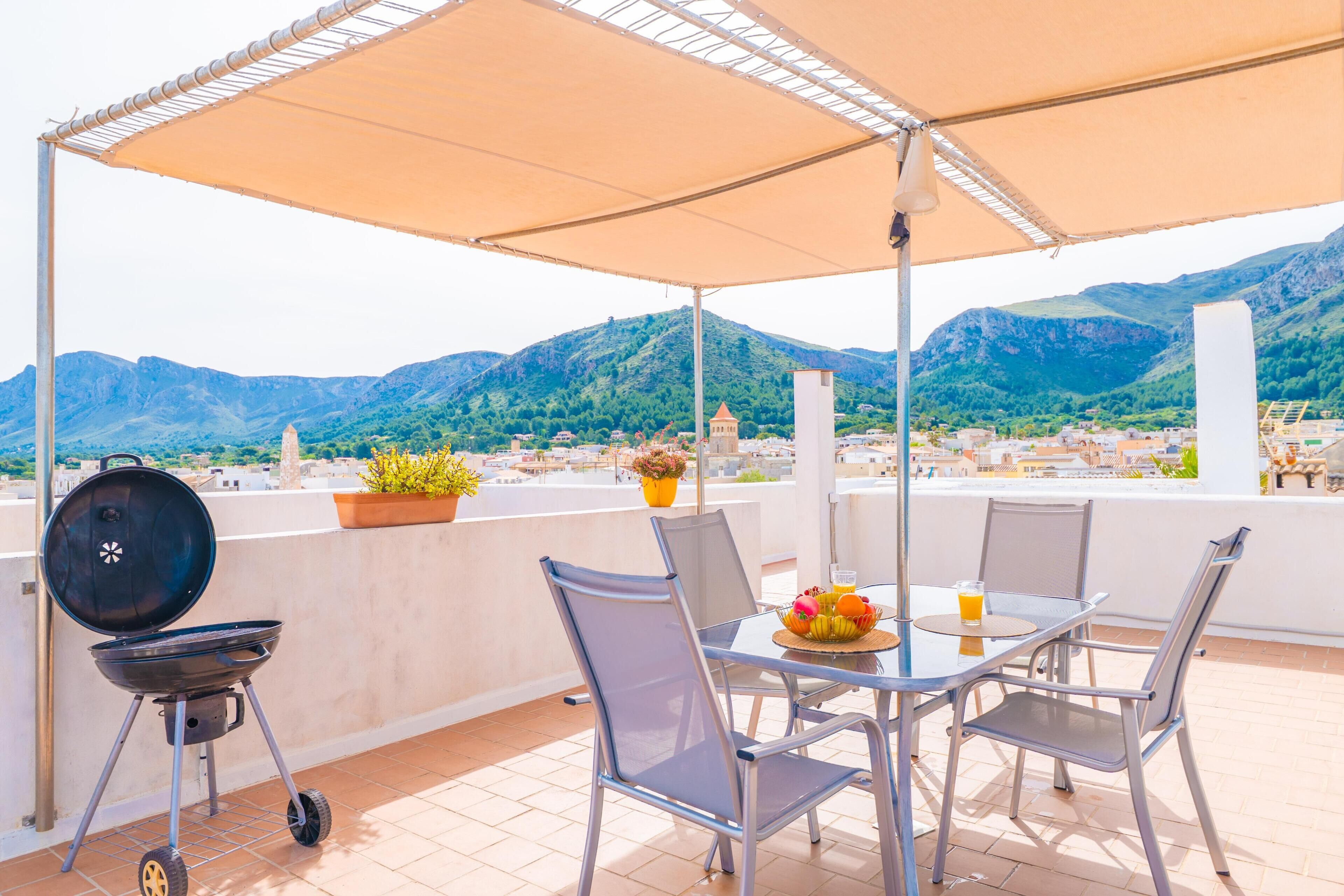 Une terrasse avec un barbecue, une table, des chaises et une vue sur les montagnes.