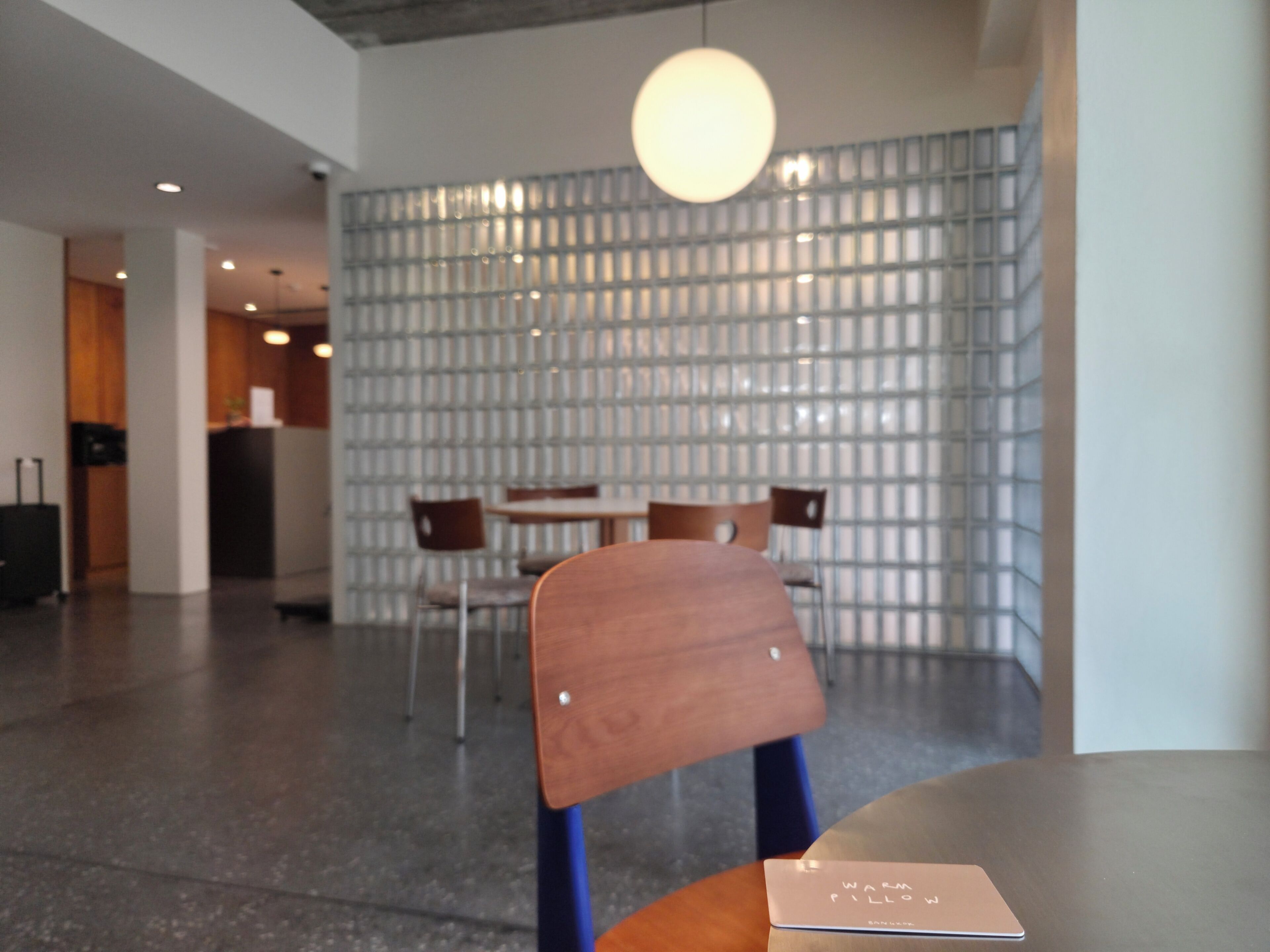 A modern interior with a round table, chairs, a wooden chair, a wall with a grid pattern, and a hanging light fixture.
