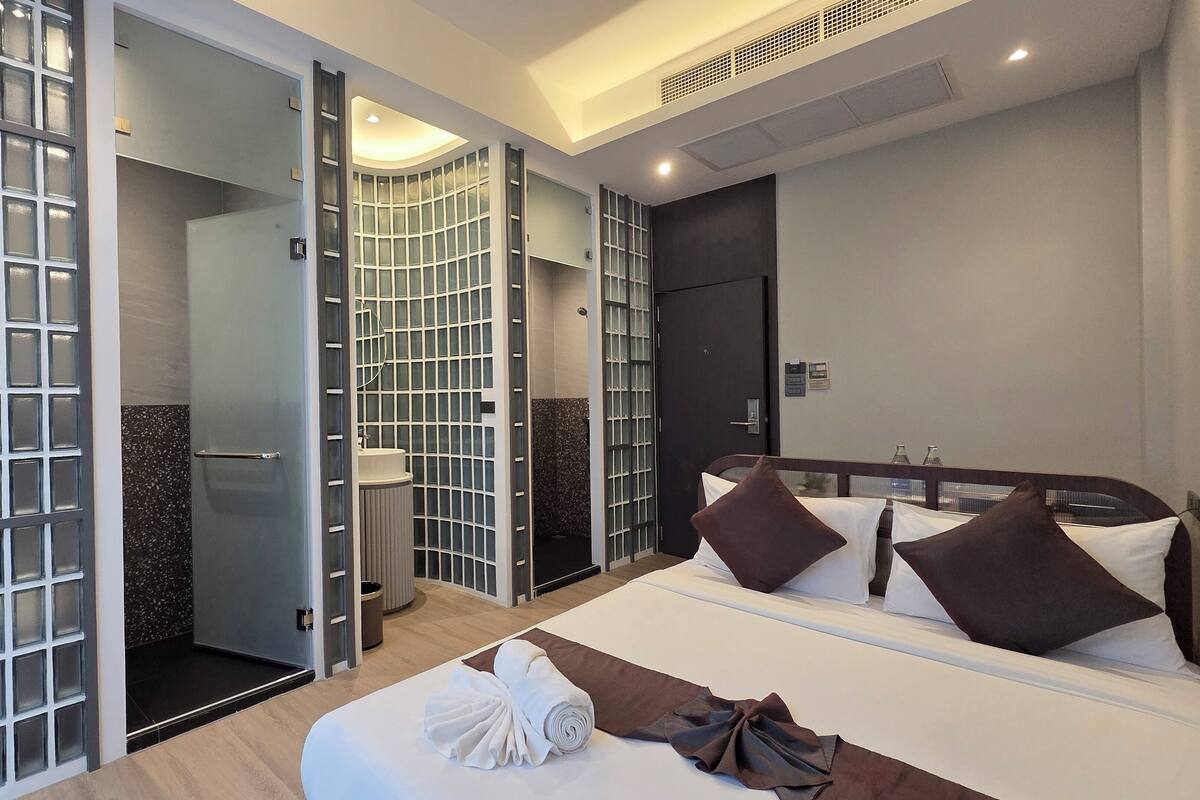 A hotel room with a bed, a bathroom with a shower, and a glass partition.