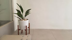 Un coin de pièce avec une plante en pot posée sur un support, une chaise blanche et un sol carrelé.