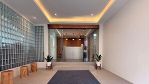 Un hall d’entrée moderne avec un mur de verre, des éléments décoratifs en bois et un grand tapis central.