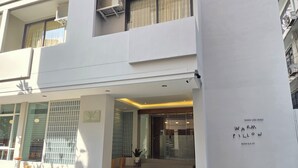 Un bâtiment moderne doté d’une entrée couverte, de climatiseurs et d’une enseigne indiquant « WARM PILLOW BANGKOK ».