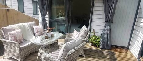 A covered patio with wicker furniture, a glass door leading to an interior space, and a wooden deck.