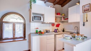 A kitchen with white cabinets, a microwave, a sink, and a window with lace curtains. - Le Fontane With View Lake (Gardone Riviera)