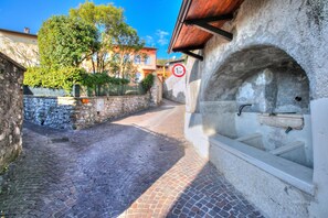 A cobblestone street with a stone wall on one side and a building with a wooden roof on the other. - Le Fontane With View Lake (Gardone Riviera)
