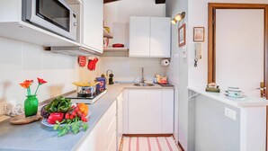 Cocina compacta con alacenas blancas, microondas, lavabo y una pequeña encimera con diversos objetos.