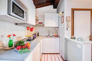A compact kitchen with white cabinets, a microwave, a sink, and a small countertop with various items. - Le Fontane With View Lake (Gardone Riviera)