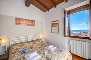 A bedroom with a bed, a window with a view, and a painting on the wall. - Le Fontane With View Lake (Gardone Riviera)