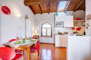 A dining area with a wooden table and red chairs, a kitchen with white cabinets, and a clock on the wall. - Le Fontane With View Lake (Gardone Riviera)