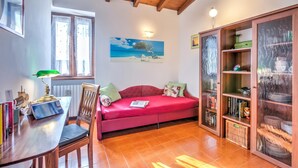 Un salón acogedor con un sofá rojo, una mesa de madera con libros, una lámpara verde y un cuadro en la pared.
