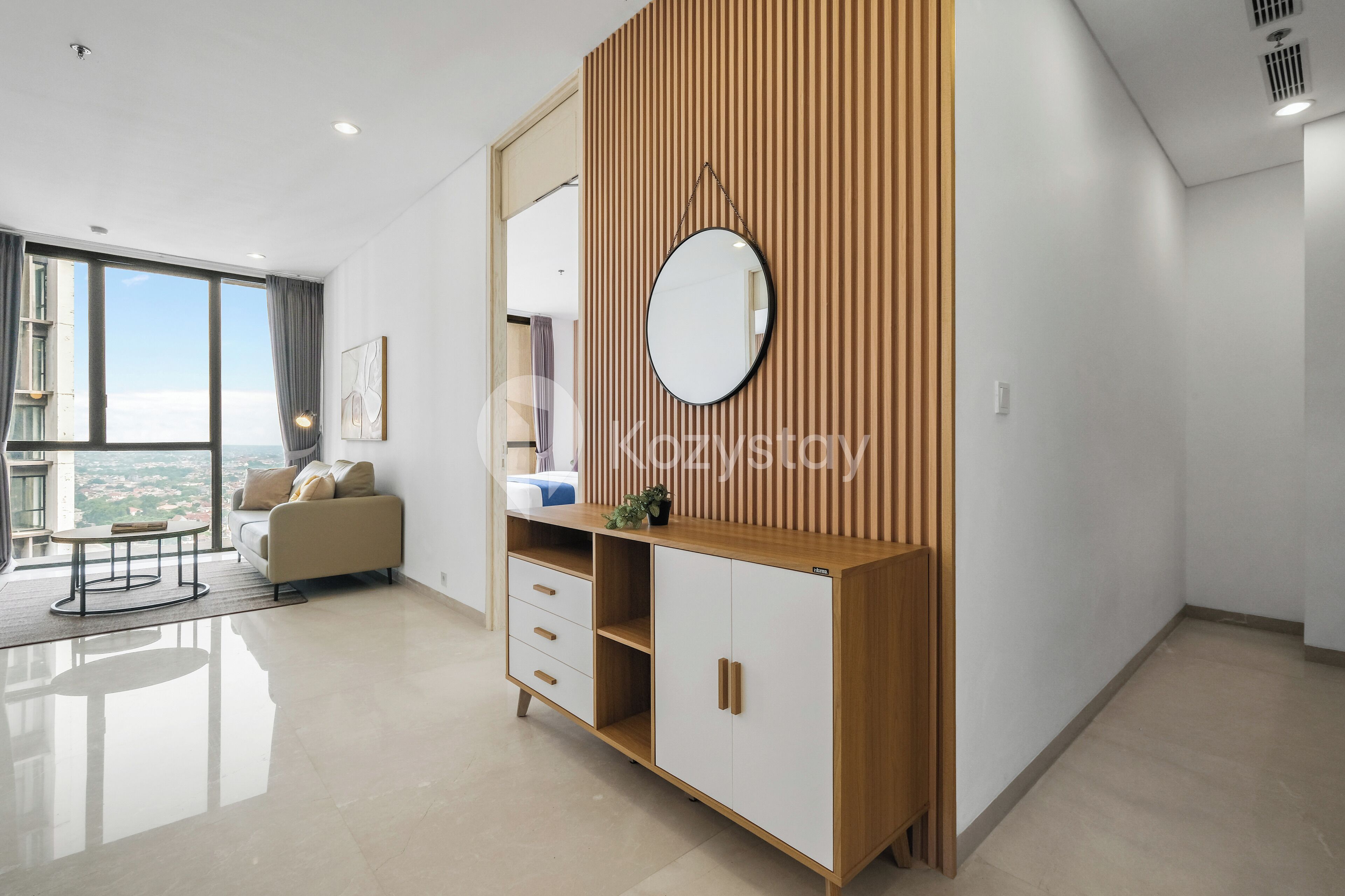 A modern living room with a large window, a sofa, a coffee table, and a wooden cabinet with a mirror.