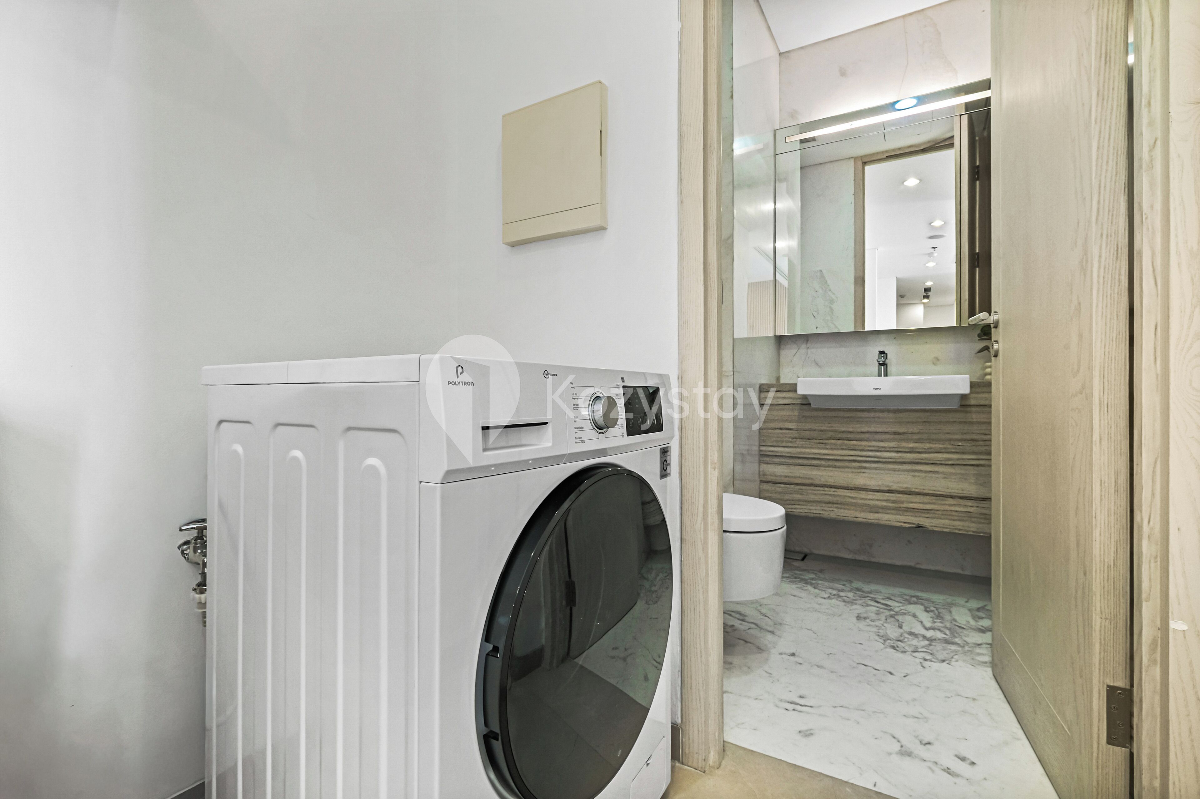A compact laundry area with a front-loading washing machine, a small sink, and a mirror above the sink.