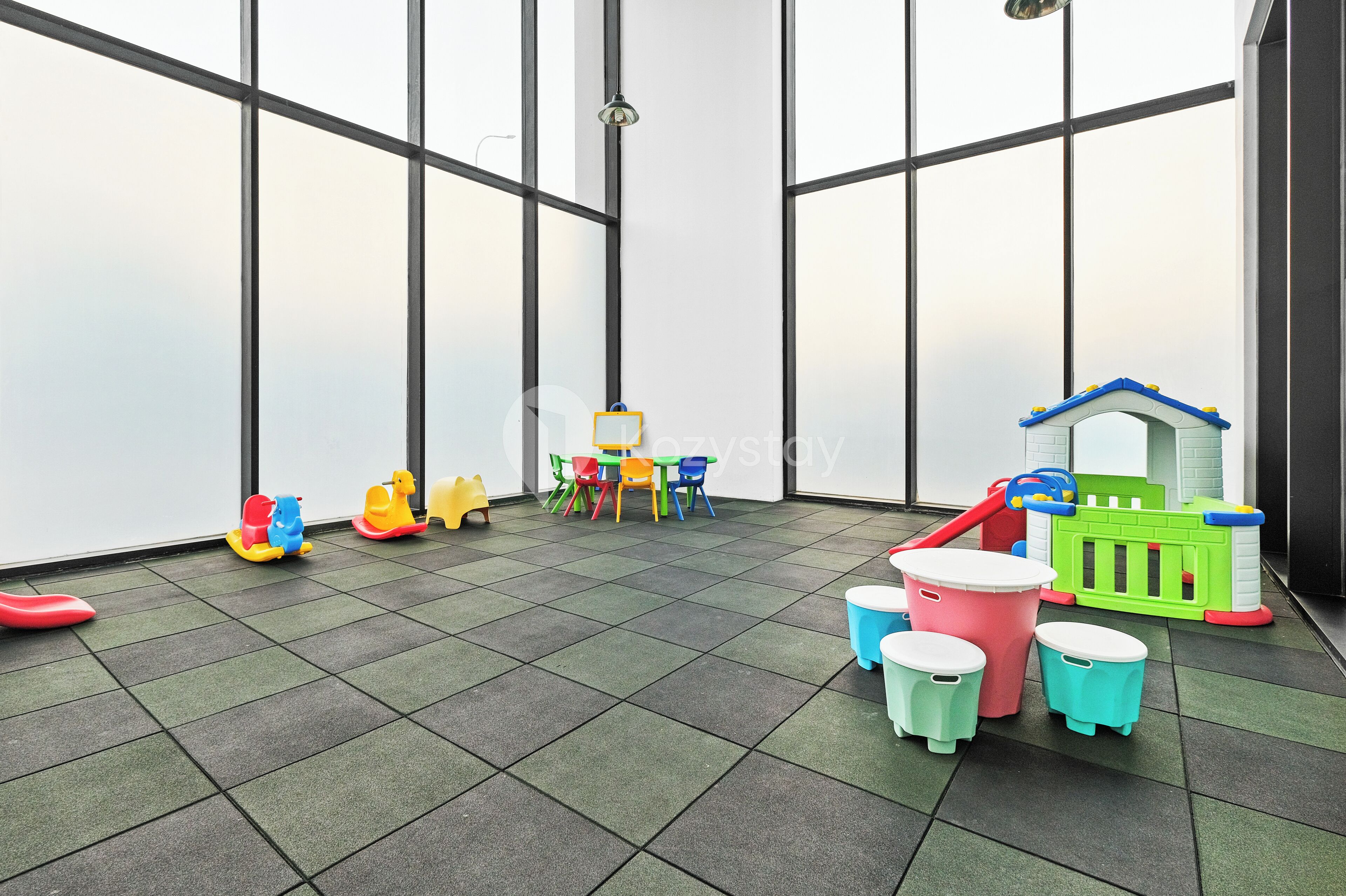 Un espace de jeux pour enfants avec une petite maison de jeu verte, des chaises colorées et une petite table.
